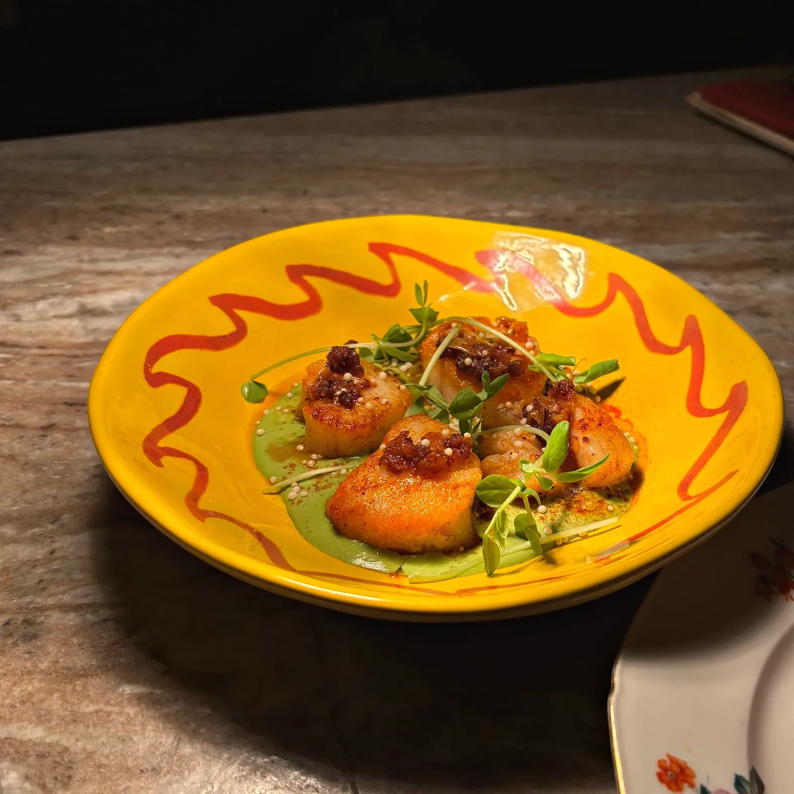 Seared scallops with herb oil and microgreens on a hand-painted plate